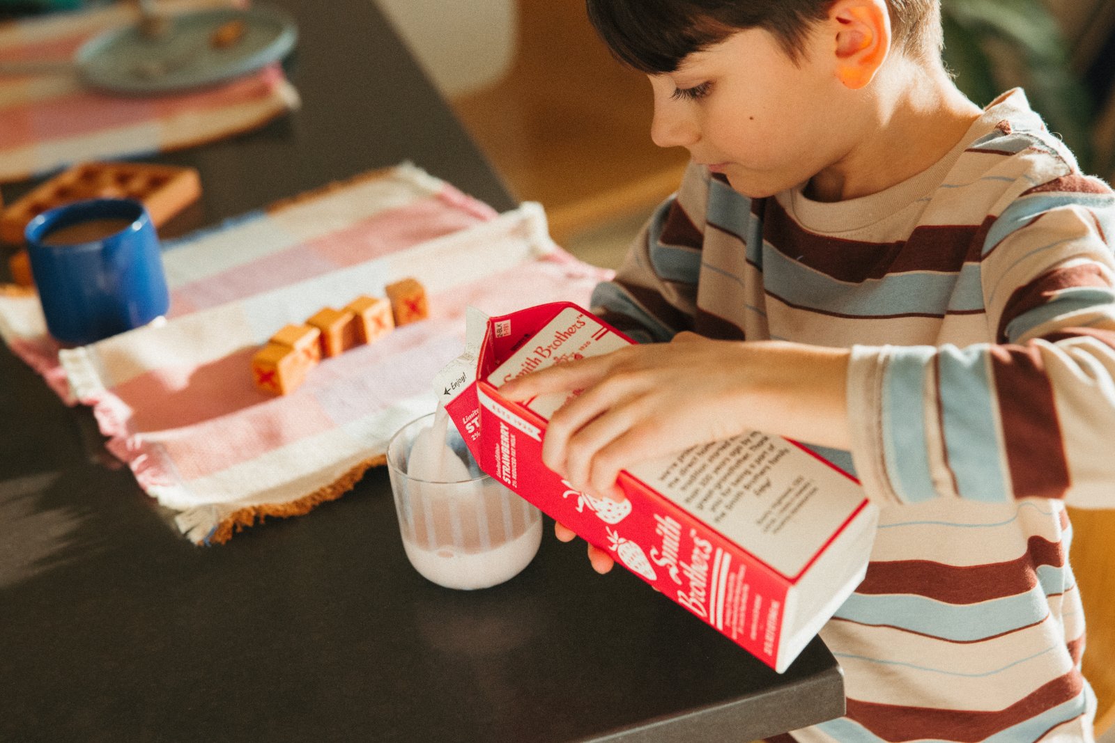 Boy pouring Smith Brothers strawberry milk at breakfast
